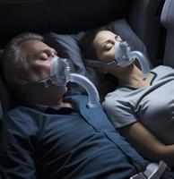 A man and a woman sleeping in bed, both wearing CPAP masks